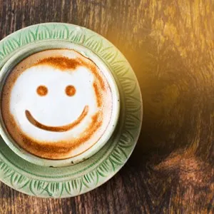 Smile of latte coffee with sunshine on wooden background